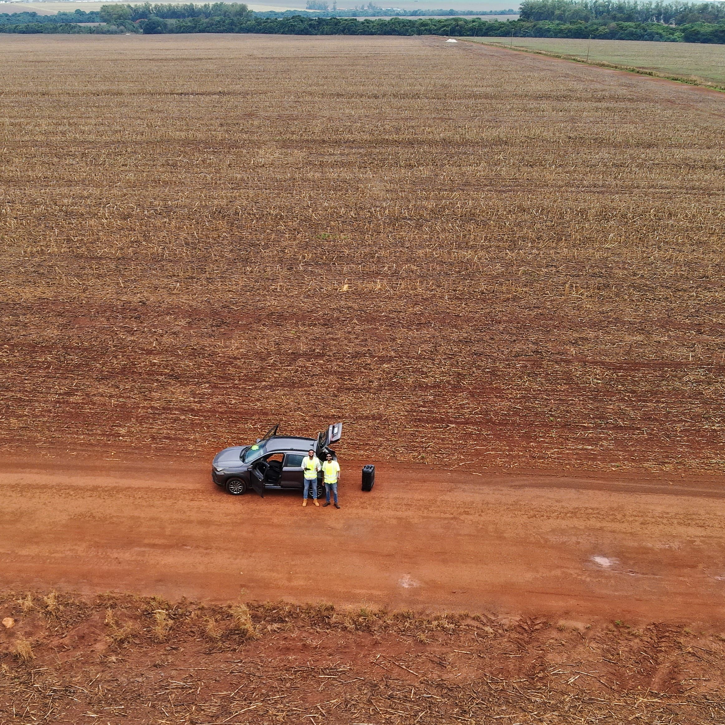 drone perspective of two people and a vehicle in the middle of a field